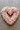A heart-shaped floral arrangement made of pink and white roses and ranunculus placed on green grass.