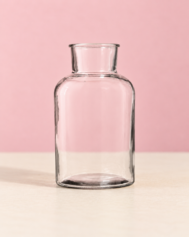 Alea clear glass vase with rounded shoulders and a narrow neck, on a neutral surface against a soft pink background