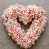 A heart-shaped floral arrangement made of pink and white roses and ranunculus placed on green grass.